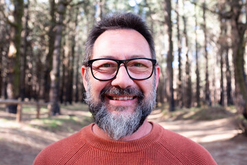 Fototapeta premium Cheerful adult happy man taking selfie picture in the woods enjoying outdoors leisure activity in national forestal park alone. Adventure and lifestyle people. High trees in background. Sustainability