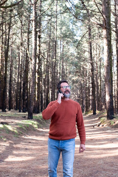 Cheerful adult happy man taking selfie picture in the woods enjoying outdoors leisure activity in national forestal park alone. Adventure and lifestyle people. High trees in background. Sustainability