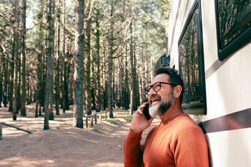 Travelers man standing outside a modern motorhome camper van enjoying destination in nature forest...