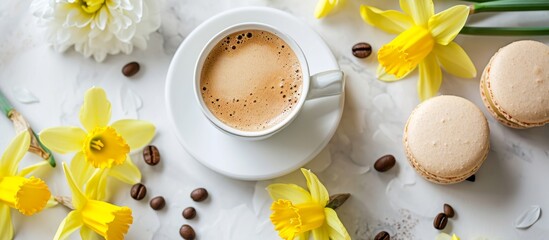 Coffee, macaron, daffodils create a bouquet on a white board.