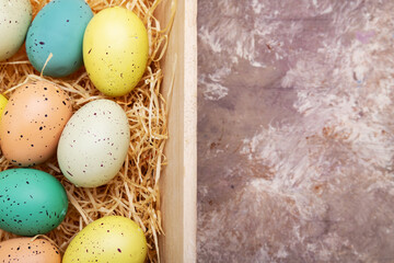Easter, colored eggs in a wooden box on straw. View from above. Space for text