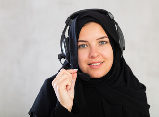 Cheerful young muslim woman wearing black traditional hijab with headset on