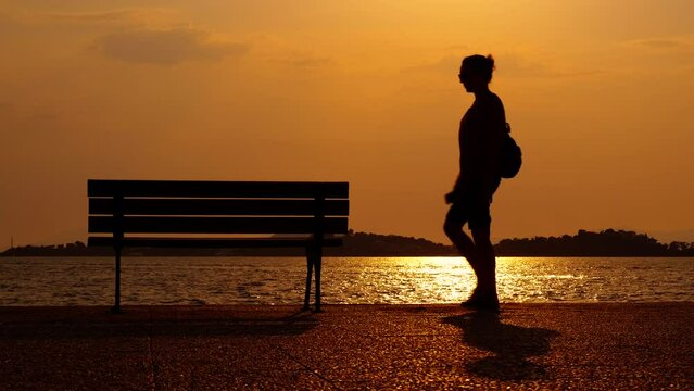 Woman promenade by evening sea bench. A man traveler silhouette walking along the waterfront and enjoy the evening time in summer.