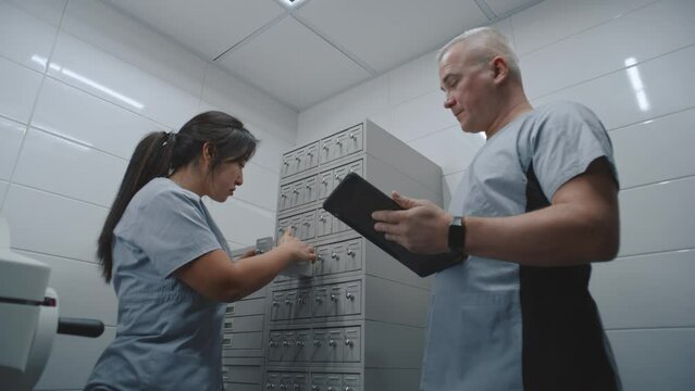 Diverse scientists check samples of blood tests or histology biological tissues analysis in medical storage cabinet with racks. Male nurse uses digital tablet computer. Modern scientific laboratory.