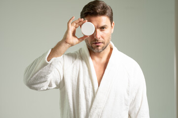 Young happy manful guy applying face cream. Close up shot of attractive man with healthy skin, applies cream for anti wrinkle or anti aging, cares of body. Beauty portrait. Body positive. Skin