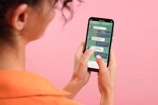 Woman texting with friend using messaging application on smartphone against pink background, closeup