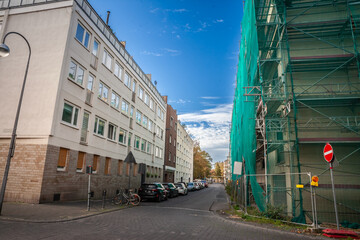 Typical german residential street with multi stories buildings and cars parked in Cologne. A construction site of a building renovation project is visible on the right.
