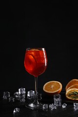 Glass of tasty Aperol spritz cocktail with orange slices and ice cubes on table against black background, space for text
