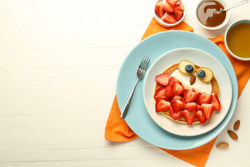 Creative serving for kids. Plate with cute owl made of pancakes, strawberries, cream, banana and almond on white wooden table, flat lay. Space for text