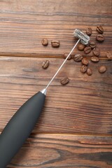 Black milk frother wand and coffee beans on wooden table, top view