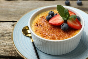 Delicious creme brulee with berries and mint in bowl on wooden table, closeup