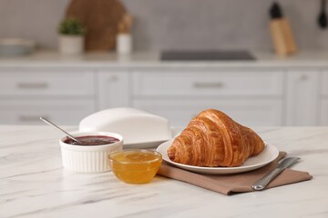 Breakfast served in kitchen. Fresh croissant, jam and honey on white table