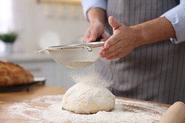 Making bread. Man sprinkling flour onto dough at wooden table in kitchen, closeup