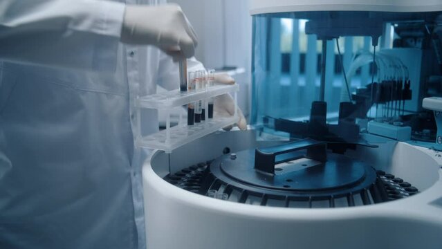 Male chemist puts blood samples from tube rack into modern automatic device for biochemical blood tests analyzing. Professional scientist works in advanced research lab. Biotechnology laboratory.