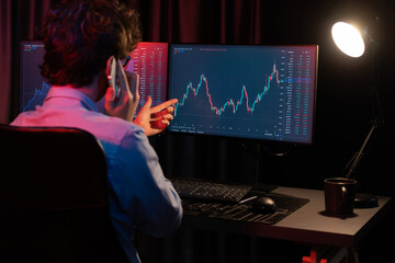 Young investor stock trader calling with broker to invest earning highest profit on current market graph online in real time at neon light modern office, monitor showing investment exchange. Gusher.