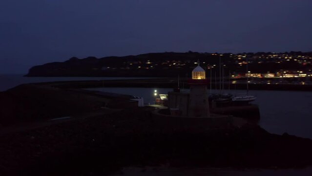 Howth Harbour view at night featuring town lights and lighthouse beacons in the foreground. Establishing shot