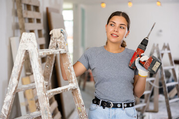 Young woman holding drill and smiling. Repair works in house.