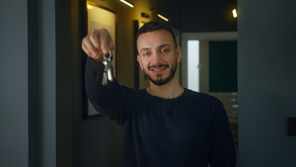 Adult homeowner man standing front the hall entrance showing key from new home at camera, smiling,...