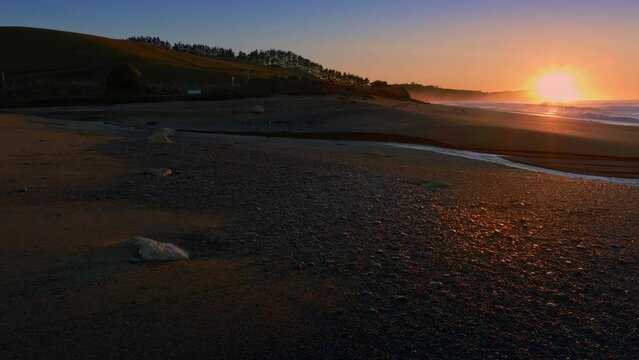 Aerial: Ocean beach surf and river in sunrise. Oamaru, Otago, New Zealand.