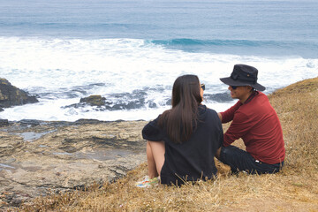 Pareja de turistas disfruta del borde de la costa, conversa ríe, observa la naturaleza.