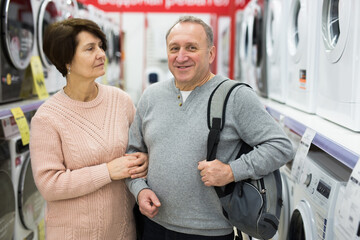 European spouses of mature age choose a washing machine in an electronics and home appliance store...
