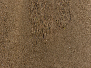 Background image of sand texture, with natural patterns partially washed away by crashing waves on a beach.