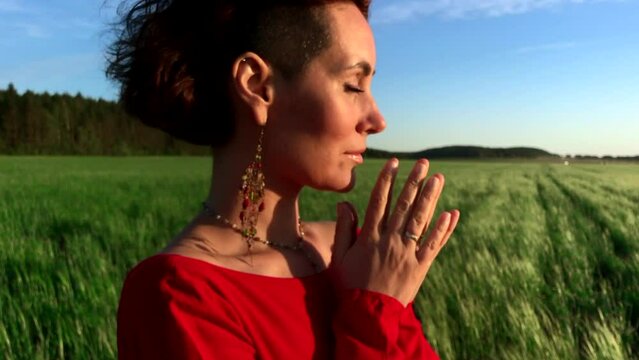  Young pretty girl woman meditating with closed eyes. Stock clip. Praying while standing in a field with a beautiful view on a windy summer day at sunset.