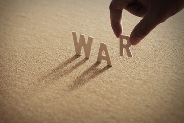 WAR wood word on compressed or corkboard with human's finger at R letter..