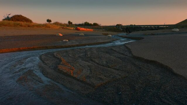 Aerial: Ocean beach surf and river in sunrise. Oamaru, Otago, New Zealand.
