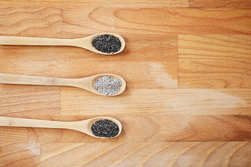 White and black Chia seeds on three spoons on a wooden board, with negative space