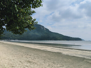 A tranquil beach scene with calm waters and a mountainous backdrop.