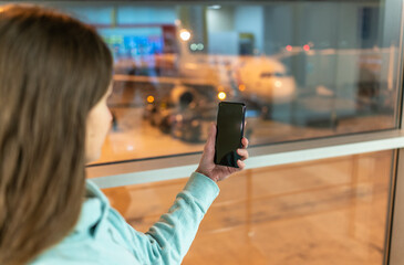 Girl holds a smartphone with a black screen close-up. Phone on the background of the airport with an airplane