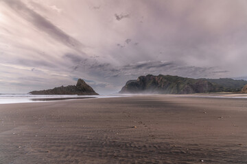 The massive black iron sand Karekare beach with picturesque rock formations out in the water. Waitakere Ranges Regional Park, Auckland, New Zealand.