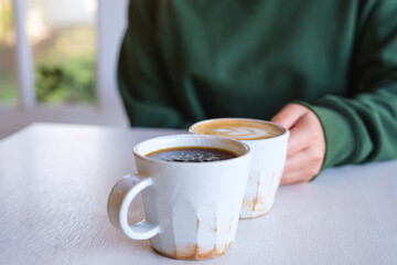 Closeup image of a woman holding and drinking coffee with friend in cafe