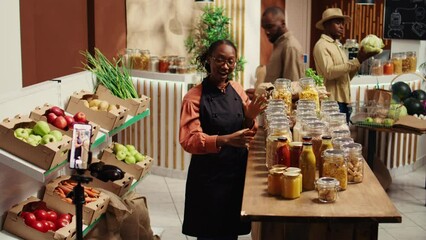 African american vendor promoting homemade sauces and honey, creating online video advertisement to present eco friendly products at zero waste supermarket. Woman recording promotional ad. Camera B.