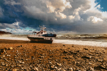 The wreck of a yacht in stormy weather. View of the beached ship. A shipwreck on the beach. An old...