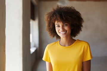A woman wearing a yellow shirt smiles directly at the camera, radiating warmth and happiness.