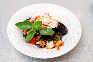 Seafood Pasta with Mussels and Fresh Basil. A plate of appetizing seafood pasta topped with mussels, shredded cheese, and fresh basil leaves, served on a white textured plate.