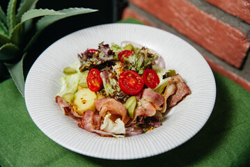 Bacon and Potato Salad with Fresh Greens. A delicious bacon and potato salad garnished with cherry tomatoes and leafy greens, served on a white ribbed plate.