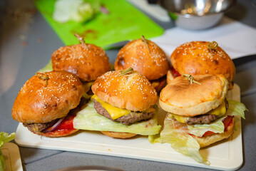 Homemade Mini Burgers with Cheese and Lettuce. A tray of delicious homemade mini burgers featuring sesame buns, cheese slices, lettuce, and tomato sauce, perfect for parties and gatherings.