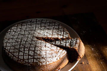 Chocolate cake on plate with a cut slice covered in icing sugar