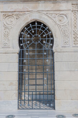 Ornate ancient stone window with a protective grille on a detailed masonry wall