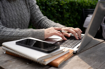 A cropped shot of a woman working remotely at a table outdoors, using a laptop computer.
