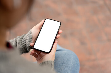 A close-up image of a woman using her smartphone while sitting outdoors. a smartphone mockup.