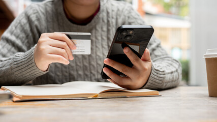 A cropped shot of a woman holding her smartphone and a credit card while sitting at a table.