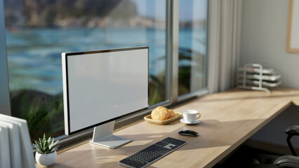 A modern office workspace with a computer mockup on a table against the window with a beach view.