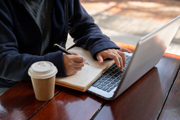 Close-up shot of a woman in a hoodie working remotely at a coffee shop in the city.