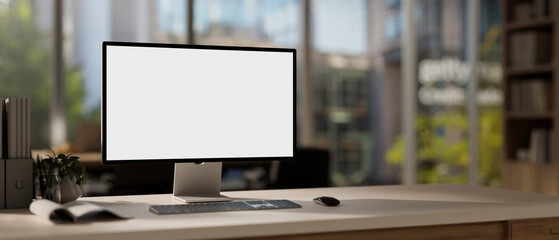 Fototapeta premium A computer mockup with a white screen and office supplies are arranged on a table in a modern office