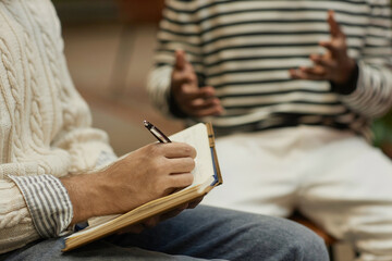 Side view closeup of psychologist taking notes during therapy session with client, copy space