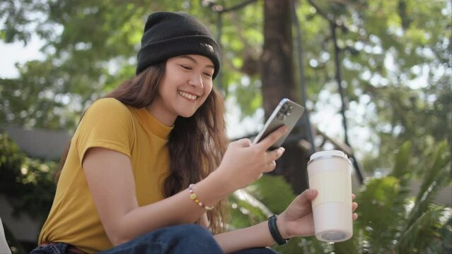 Gen Z eco go green woman asia sit happy relax at tree public park city life enjoy typing mobile phone drink coffee bottle use reuse tote bag care save the earth planet net zero waste clean future hope